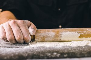 Un homme roule de la pâte à pizza sur une table farinée avec un rouleau à pâtisserie, créant une base fine et uniforme.